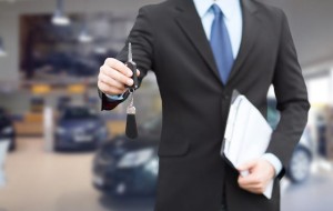 auto business, car sale, gesture and people concept - close up of businessman or salesman with documents giving car key over auto show background